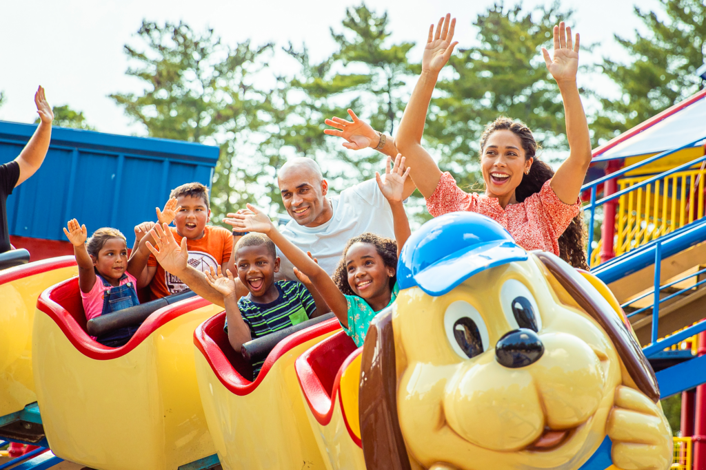A family rides the Howler roller coaster. They're smiling and have their hands in the air.