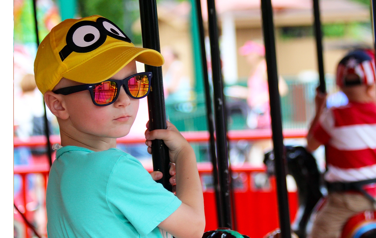 A young boy in a hat and sunglasses strikes a serious pose on Prancer's Merry-Go-Round at Holiday World & Splashin' Safari in Santa Claus, Indiana.