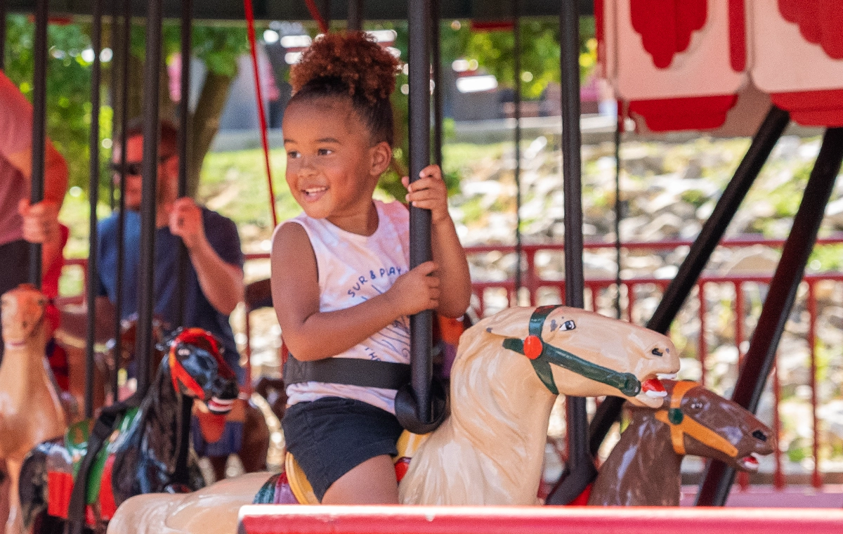 A small girl with beautiful curls smiling on Prancer's Merry-Go-Round at Holiday World & Splashin' Safari in Santa Claus, Indiana.