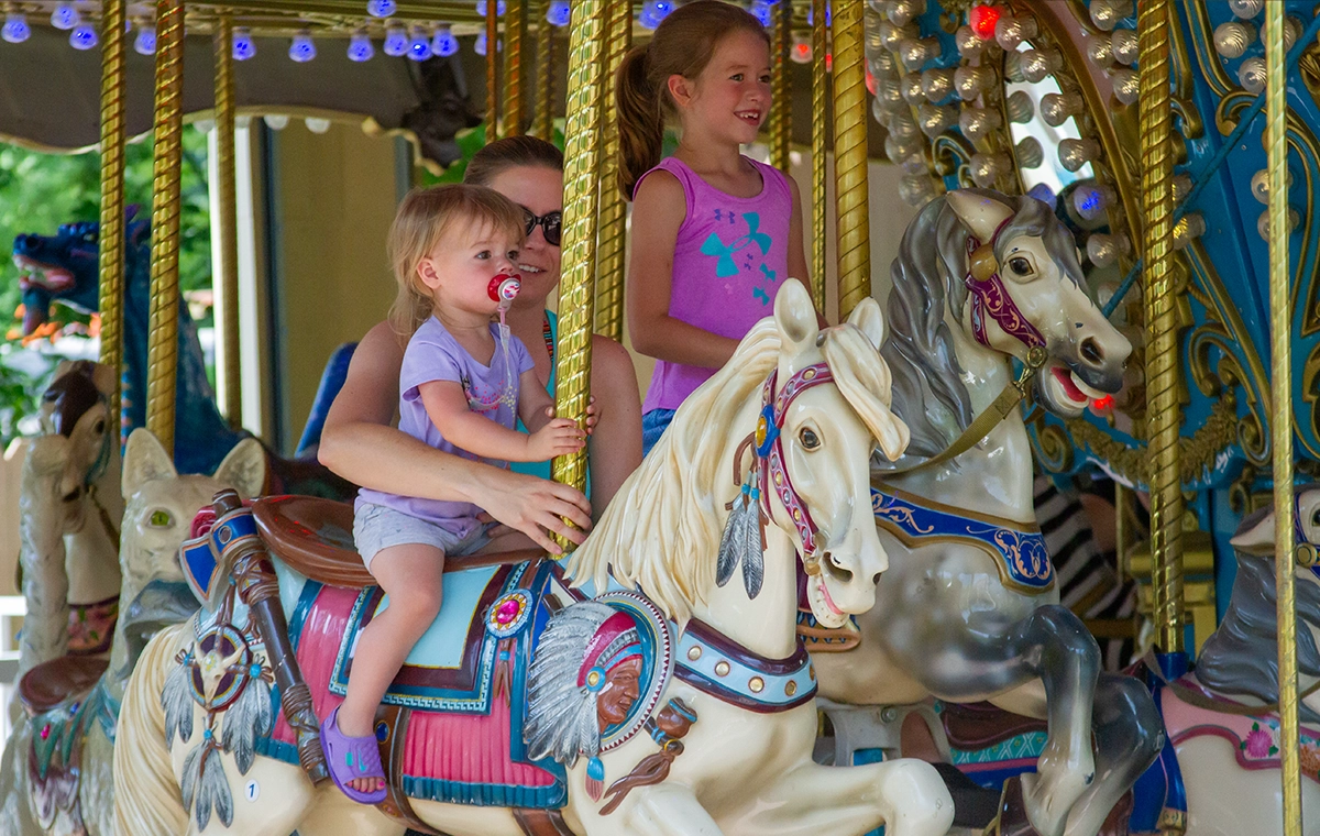 A mom helps her toddler stay steady on a horse while a young girl rides beside on Star Spangled Carousel at Holiday World & Splashin' Safari in Santa Claus, Indiana.