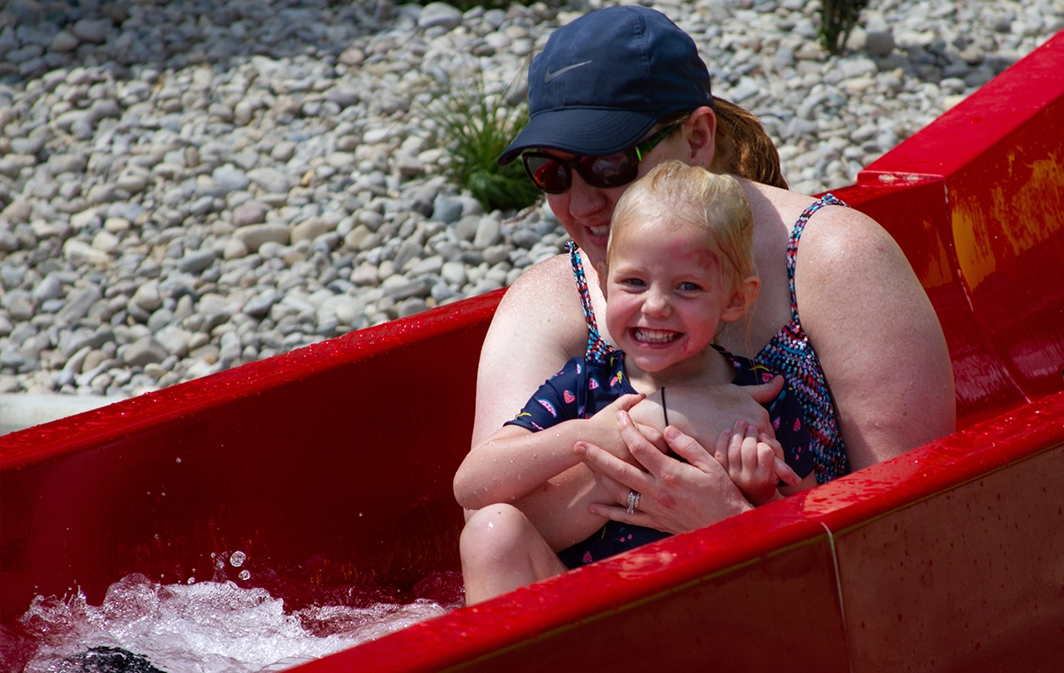A mom and daughter smile and slide down the red slide together of Tembo Falls at Holiday World & Splashin' Safari in Santa Claus, Indiana.