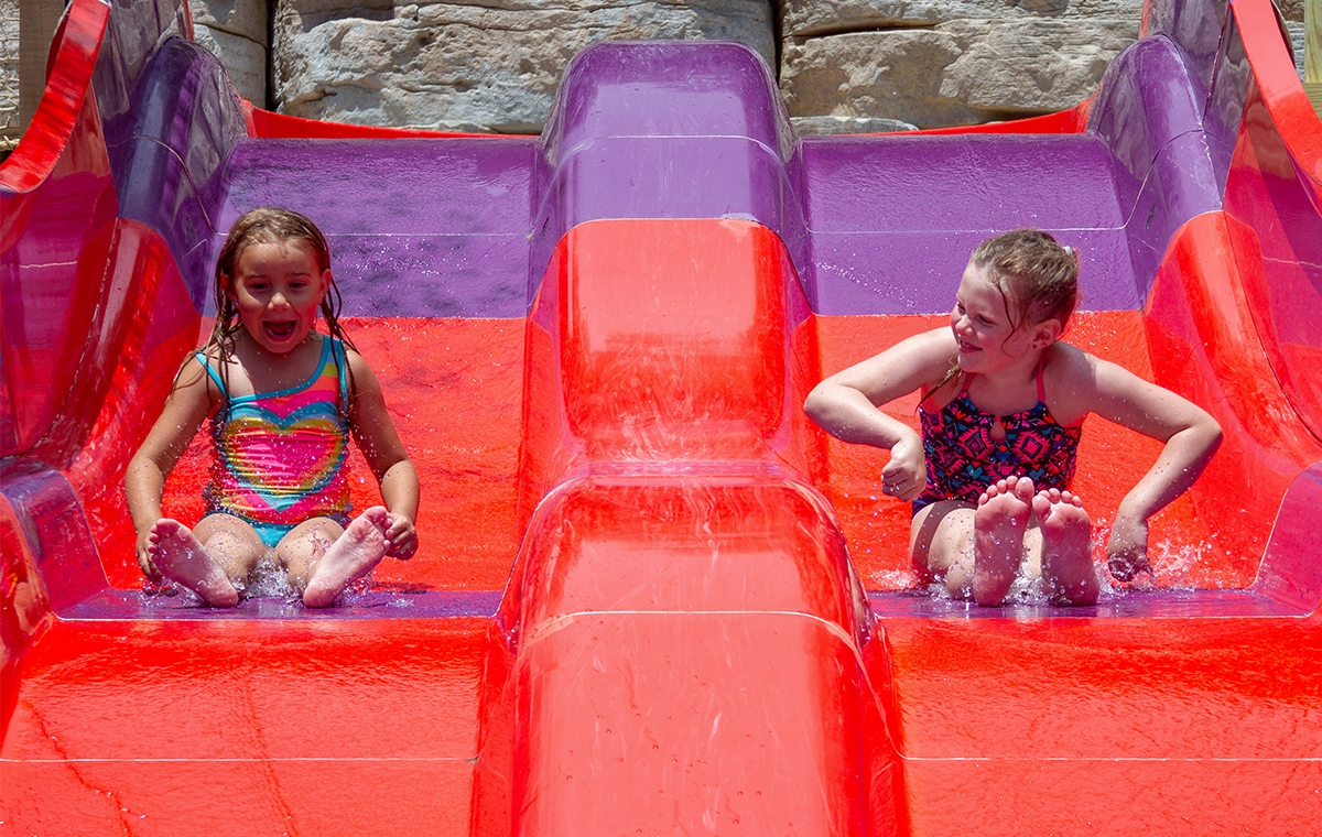 Two young girls race down a side-by-side slide at Tembo Falls at Holiday World & Splashin' Safari in Santa Claus, Indiana.