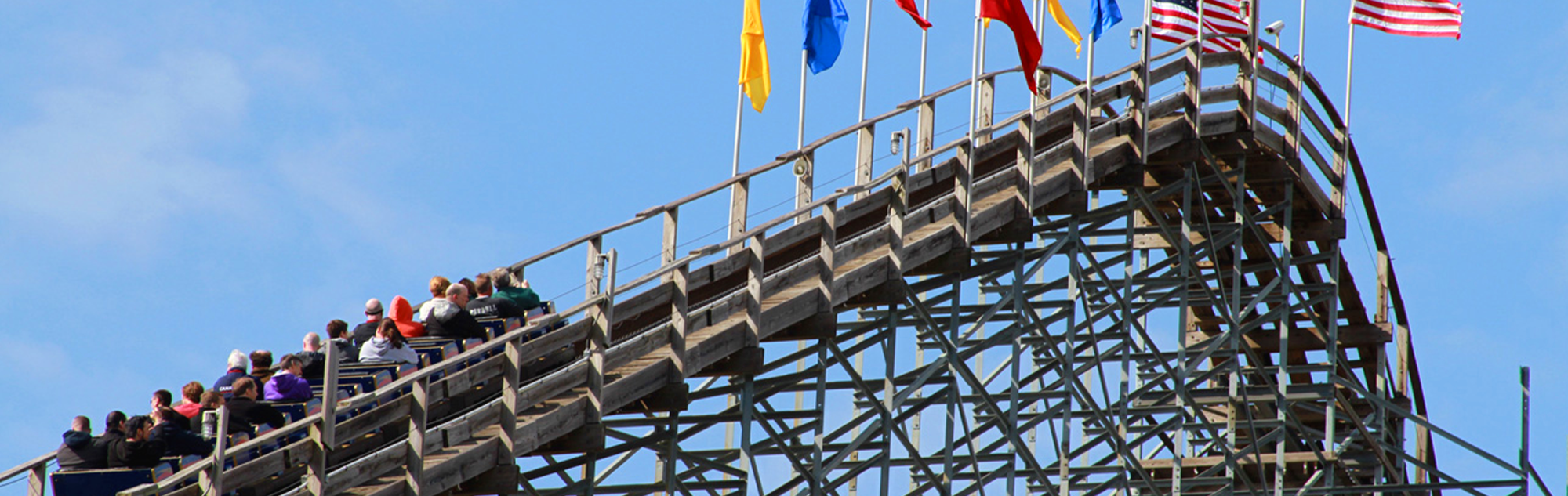 A train on The Voyage roller coaster is seen climbing the lift hill. It heads to the right as you can see colored flags and the American flag waving in the wind.