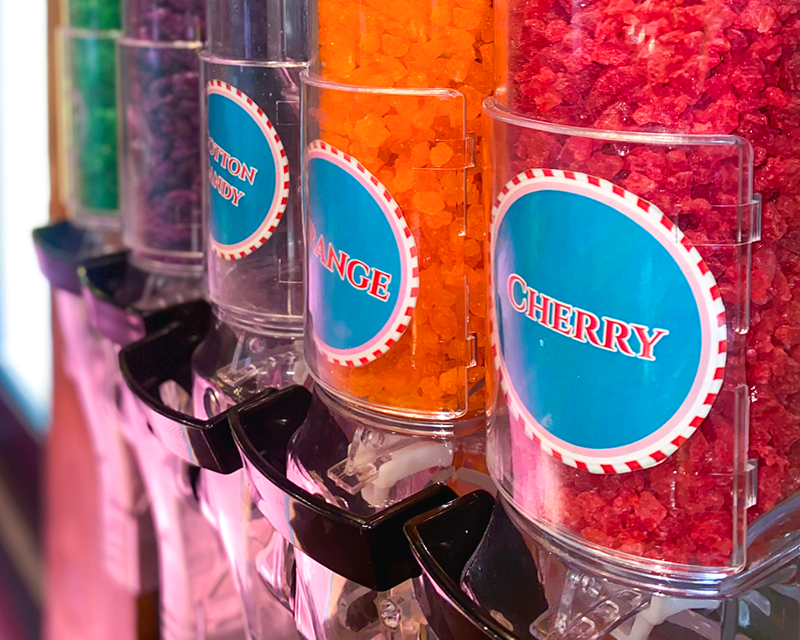 Tubes of self-serve candy dispensers featuring labels for Cotton Candy, Orange, and Cherry.