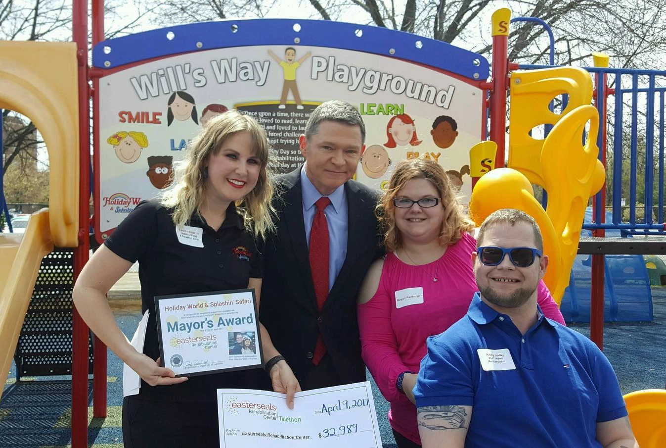 Lauren Crosby, 4th Generation Owner, poses in front of Will's Way Playground, an accessible play structure, with representatives of Easterseals Rehabilitation Center in Evansville, Indiana.