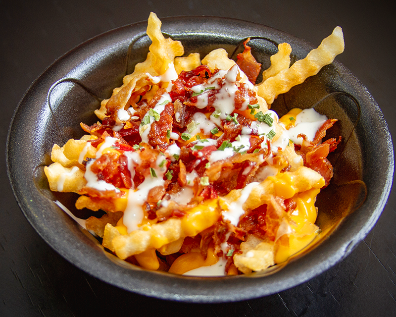 A bowl of french fries with cheese, bacon, and ranch from SnackHouse.