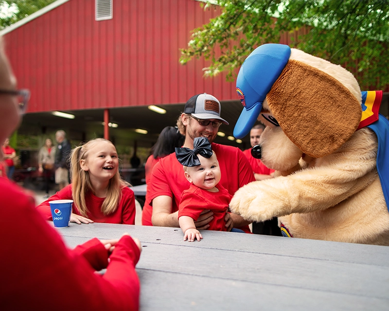Holidog plays with an infant while their family attends a Company Picnic at Holiday World.