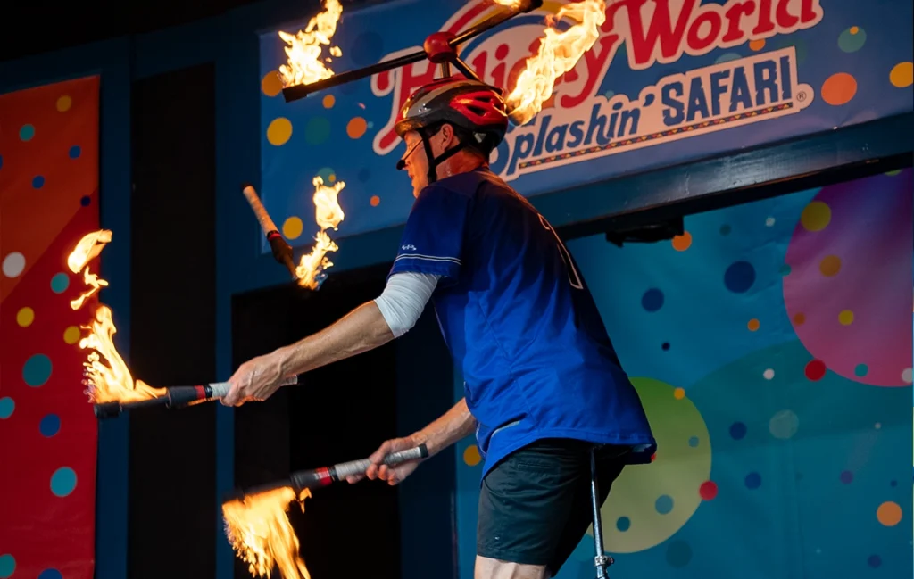 Matt Jergens juggling fire batons while riding a unicycle during the Out of Hand Comedy Juggling Show at Holiday World.