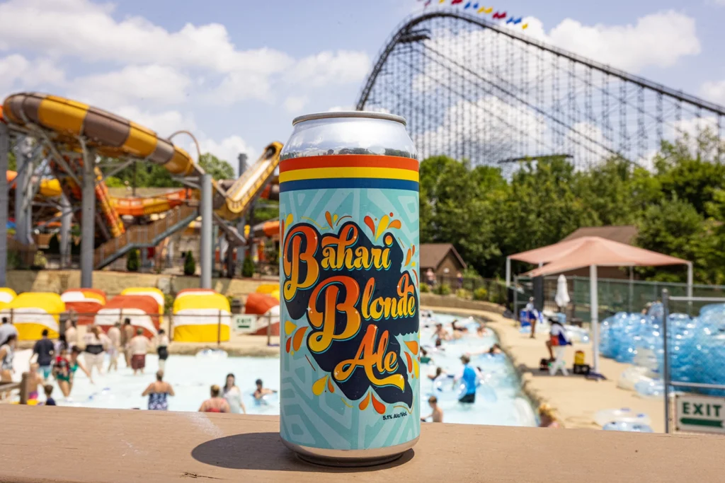 A can of custom-brewed Bahari Blonde Ale in front of Bahari River with Cheetah Chase and The Voyage's lift hill in the background.