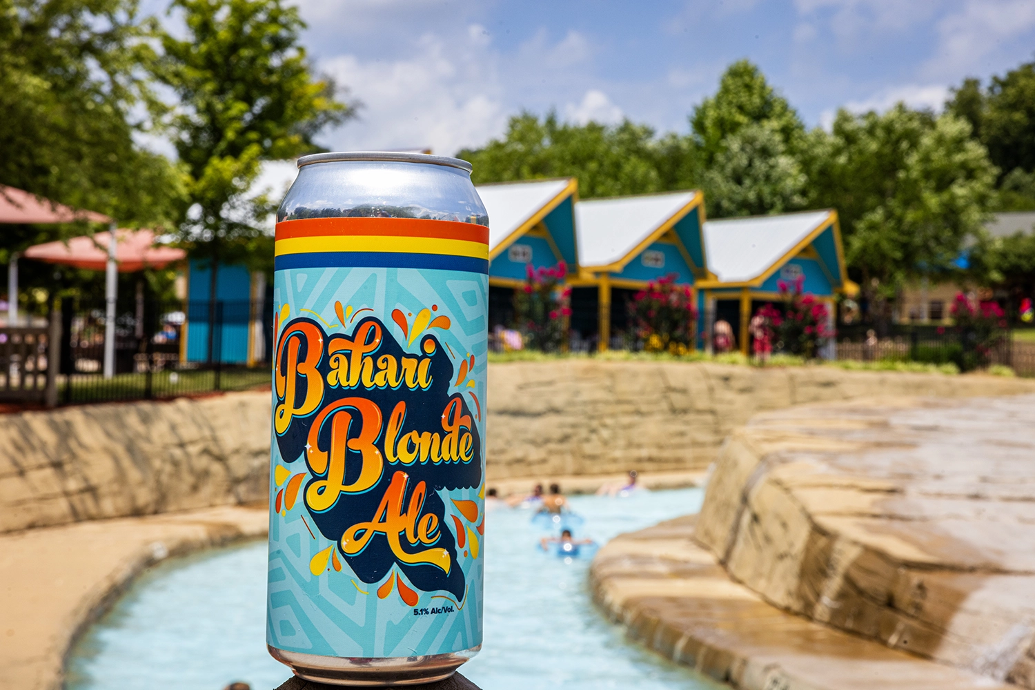 A can of custom-brewed Bahari Blonde Ale in front of Bahari River with a row of Cabanas in the background.