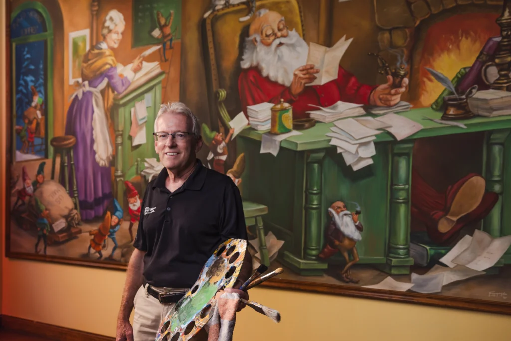 Rick Emmons, Holiday World & Splashin' Safari's painter, poses with paintbrushes and palette in front of one of his murals.