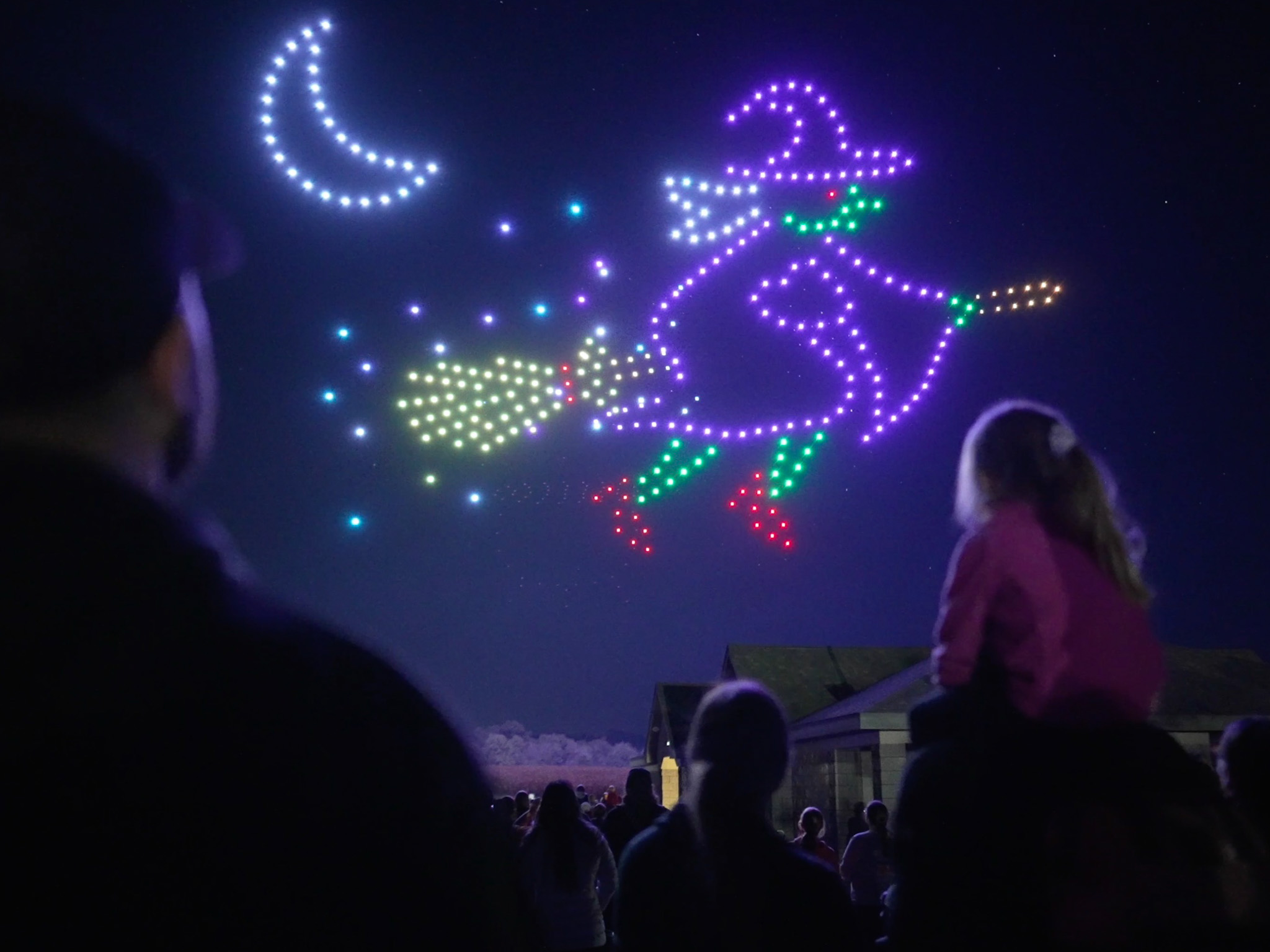 A young girl sits on her dad's shoulders watching Halloween in the Sky - as a witch and moon are displayed in drones in the sky.