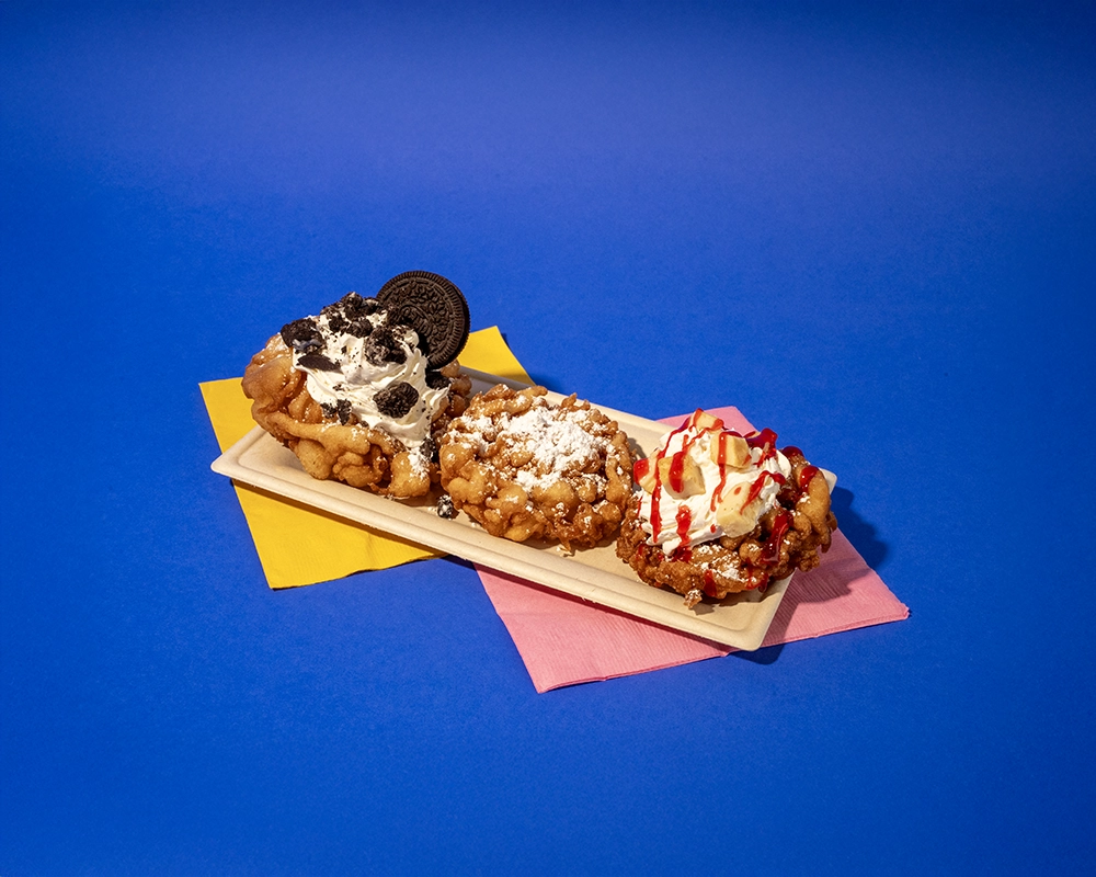 A Funnel Cake Flight of three mini-funnel cakes including a Classic, Cookies & Cream, and Strawberry Cheesecake.