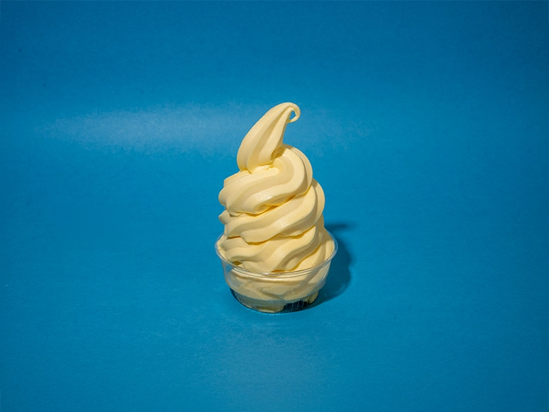 A cup of Pineapple Dole Whip on a light blue background.