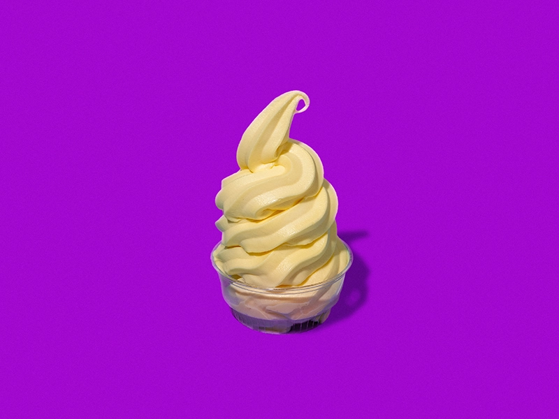 A cup of Pineapple Dole Whip on a pink background.